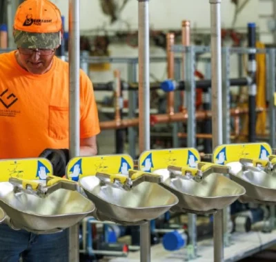 Plumbing technician assembling stainless steel emergency eye wash stations in a commercial shop environment.