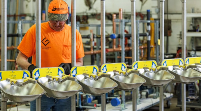 Plumbing technician assembling stainless steel emergency eye wash stations in a commercial shop environment.